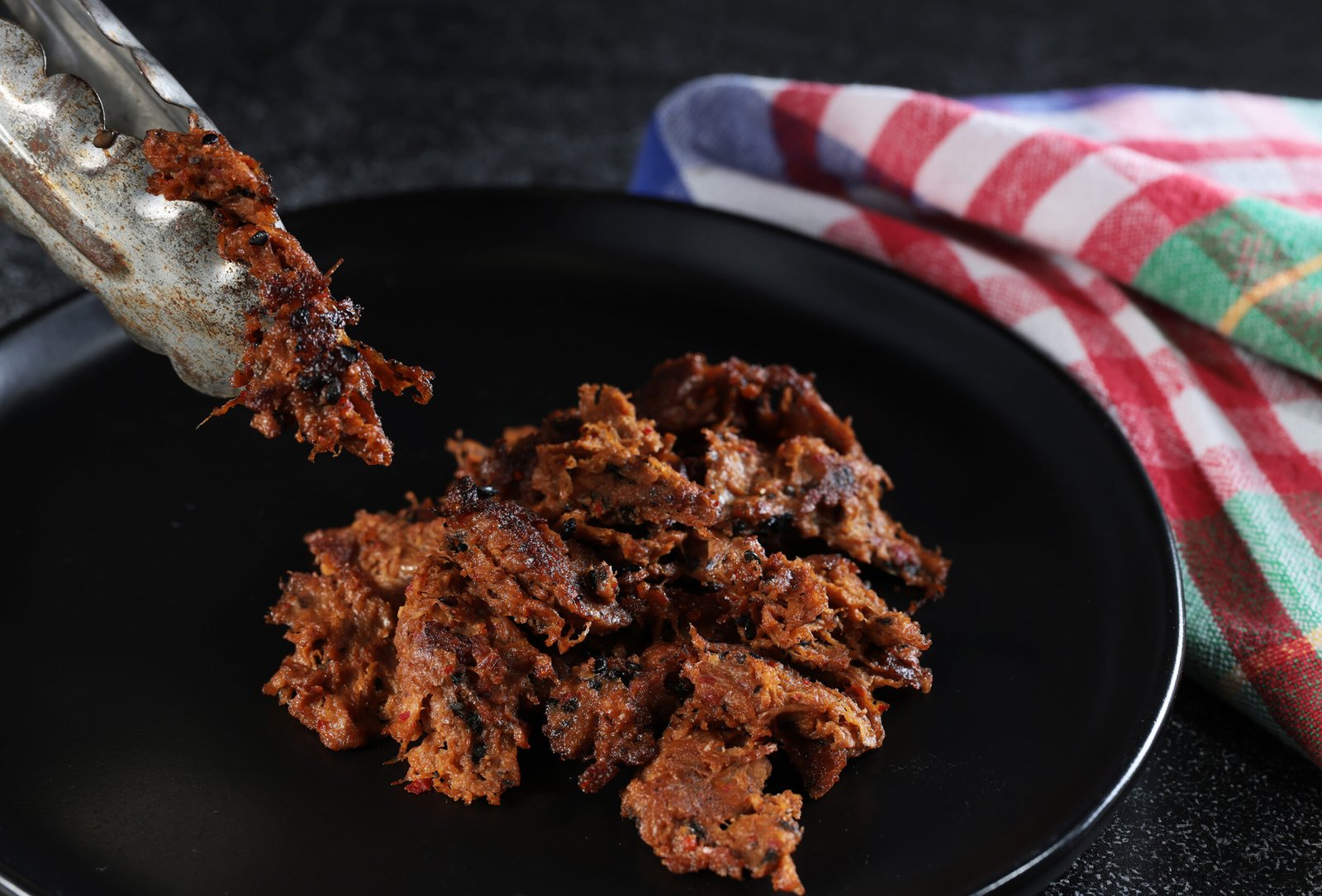 Harvest Shreds on a black plate with tongs.